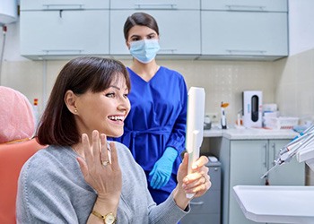 Happy dental patient holding mirror, admiring her smile