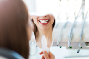woman looking at new smile in the mirror at dentist office