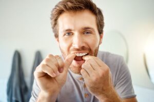 Man standing in bathroom, carefully flossing his teeth